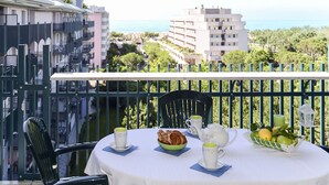 Un balcon avec une table préparée pour le thé, une chaise et une vue sur la mer et les bâtiments.