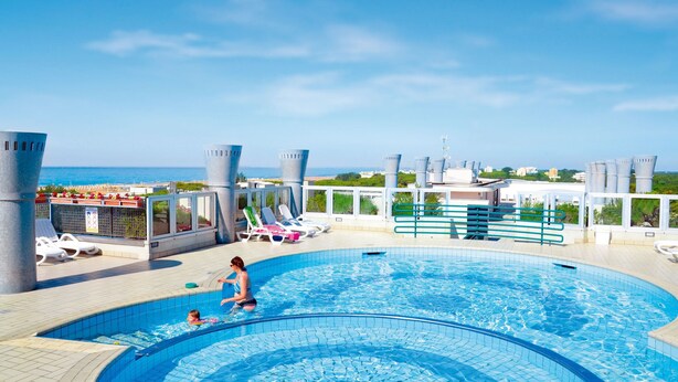 Une piscine sur le toit offrant une vue sur la mer, des chaises longues et un design architectural moderne.