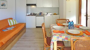 Eine kleine Küche mit weißen Schränken, einem Kühlschrank und einem Esstisch, gedeckt mit Tellern, Gläsern und einer bunten Tischdecke.