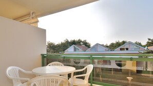 Ein Balkon mit Tisch und Stühlen, einem grünen Geländer und Blick auf Häuser im Hintergrund.