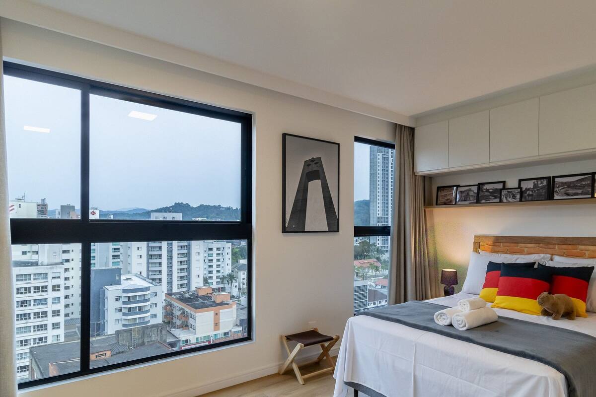 A hotel room with large windows, a bed with a brick headboard, and a city view.