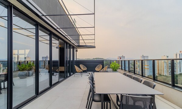 Una terrazza sul tetto con un tavolo lungo e sedie, ampie finestre e vista sulla città.