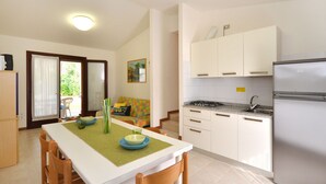 A compact kitchen with white cabinets, a stainless steel refrigerator, and a dining area with a table and chairs. - Villaggio Paradiso by Interhome (Bibione)
