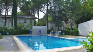 A rectangular swimming pool with a tiled deck, surrounded by trees and a building. - Villaggio Paradiso by Interhome (Bibione)