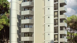Un edificio residencial moderno de varios pisos con balcones, techo plano y un área verde circundante.