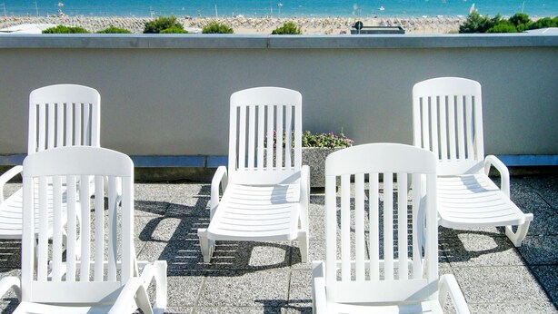 Tres sillones blancos mirando a una playa con vista despejada al océano y algunos veleros.