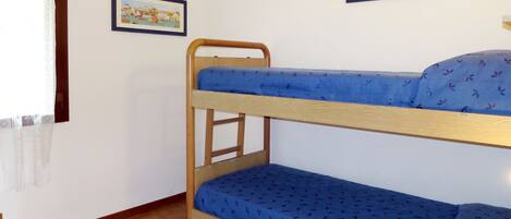 Ein Mehrbettzimmer mit zwei gerahmten Bildern an der Wand, einem Fenster mit Vorhang und einem Fliesenboden.