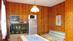Cocina compacta con paredes de madera, una mesa de comedor, sillas, un microondas, un refrigerador y un televisor.