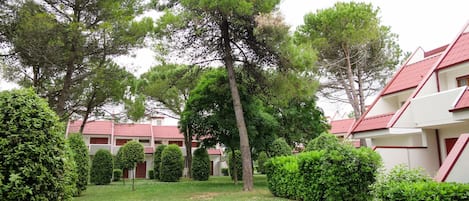 A courtyard with neatly trimmed hedges, a grassy lawn, and a row of buildings with red roofs.