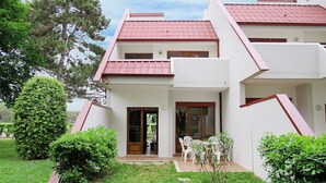 Un bâtiment à deux étages, doté d’un toit recouvert de tuiles rouges et de murs blancs. On y trouve une petite cour avec des chaises et une table en plastique blanc.
