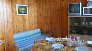 Une pièce aux murs lambrés, avec un canapé, une table à manger dressée avec des assiettes, des verres et des couverts, et un téléviseur posé sur une étagère.