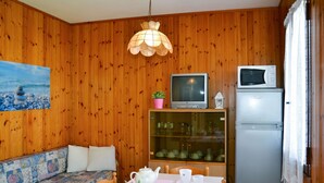 Une pièce chaleureuse avec des murs en bois, un canapé, une table à manger avec des chaises, un téléviseur, un four à micro-ondes et un réfrigérateur.