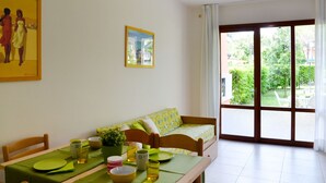 Un comedor con una mesa dispuesta para dos personas, un sofá y vistas de un jardín a través de un ventanal.