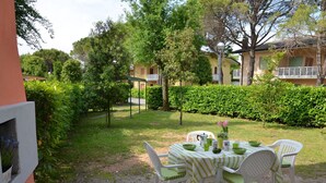 Un patio con una mesa y sillas, rodeado de vegetación y un edificio al fondo.