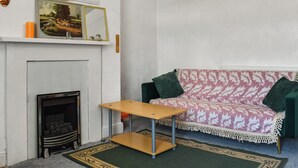 Una habitación con chimenea, un sofá, una mesita y un espejo decorativo.