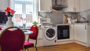 Una cocina compacta con armarios blancos, microondas integrado, lavadora y estufa.