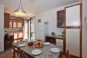 A kitchen with granite countertops, wooden cabinets, a refrigerator, and a dining table set for four.