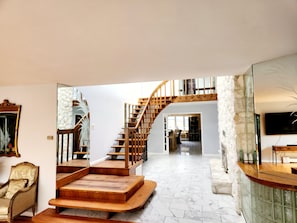 A spacious living area with a wooden staircase leading to a loft, a large mirror, and a television mounted on the wall.