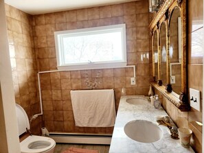 A bathroom with a toilet, sink, and bathtub. There is a window above the toilet, a towel hanging on a rack, and a mirror with a decorative frame.