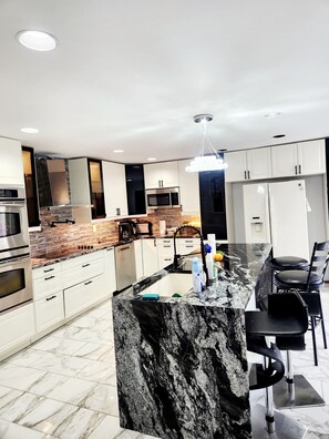 A modern kitchen with white cabinets, a black marble island, stainless steel appliances, and a hanging light fixture.