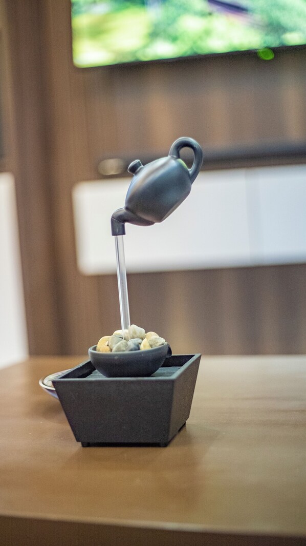 A small, dark-colored, square-shaped container with a handle on top, placed on a wooden surface. - Joshean fully furnished Apartments (Kampala)