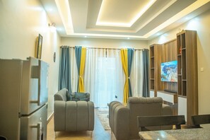 A modern living room with a sofa set, a television, and a wooden cabinet. - Joshean fully furnished Apartments  (Kampala)