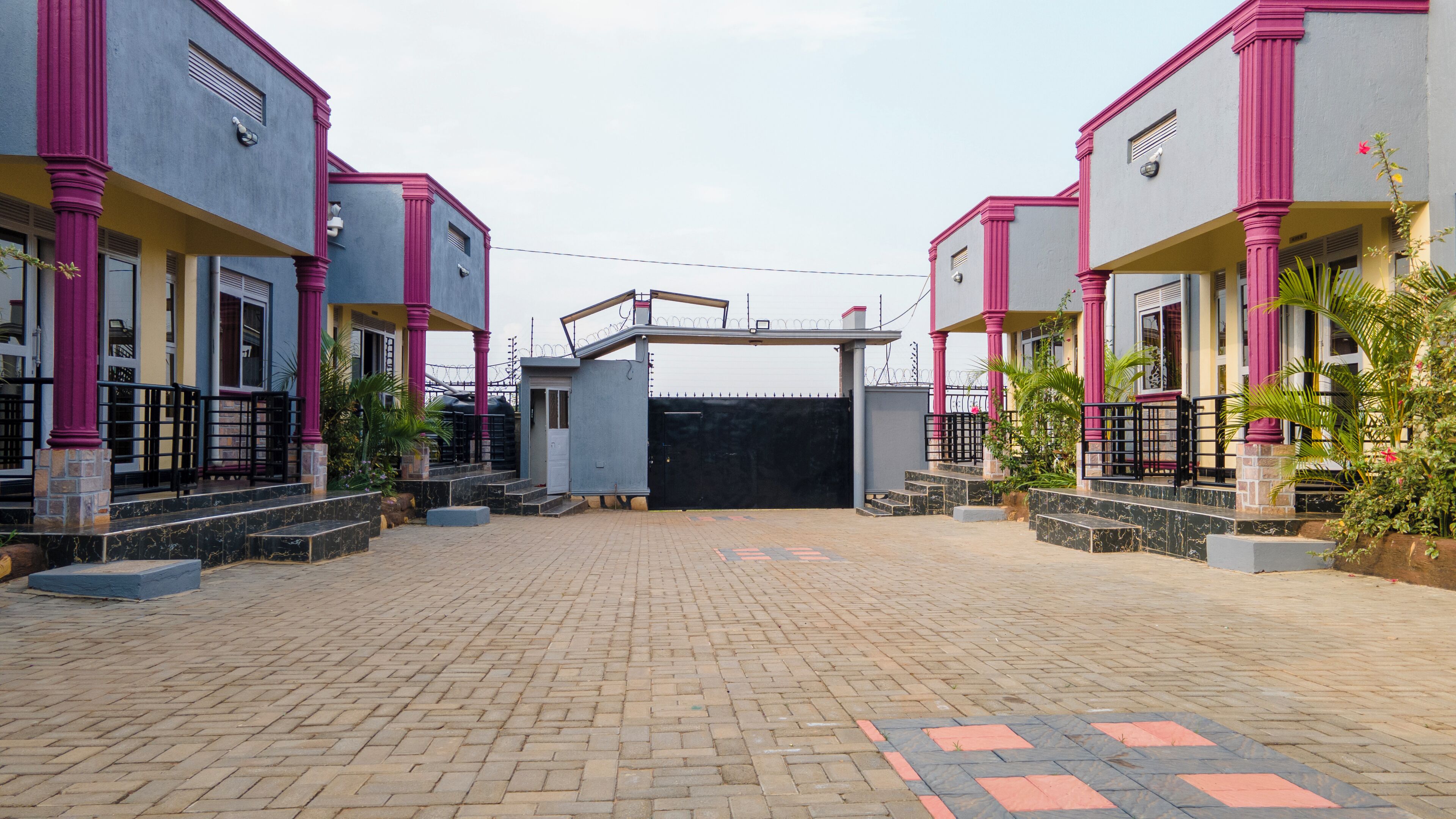 A gated entrance to a residential area with two-story houses, paved walkway, and security gate.