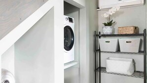 Een wasruimte met een wasmachine, planken met opbergbakken en een houten tafel.