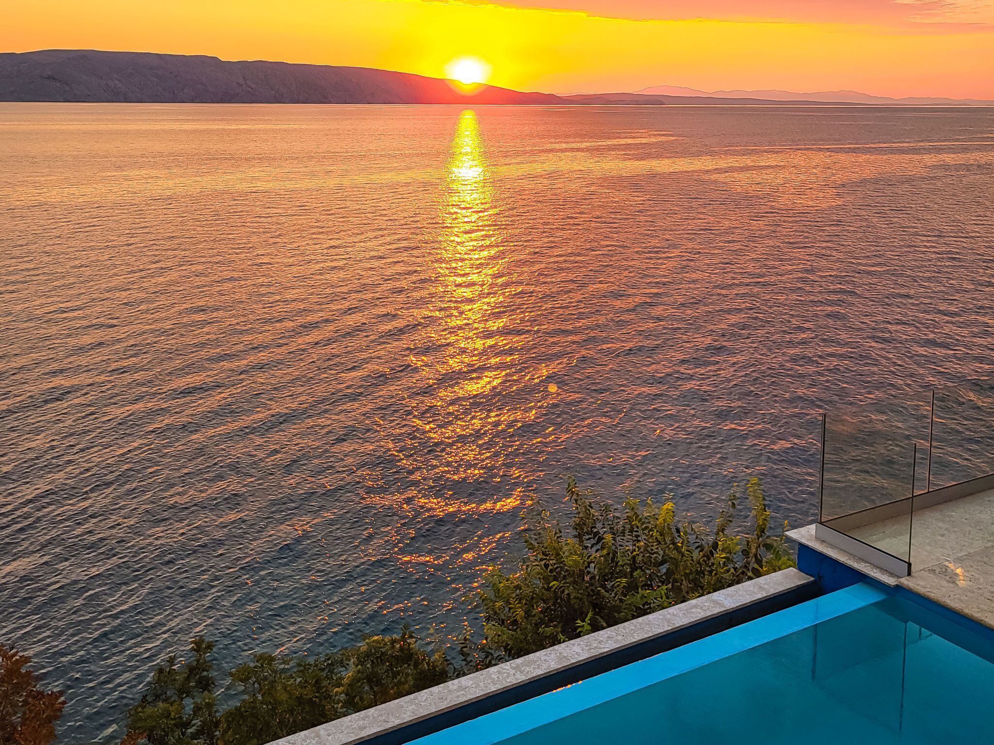 A poolside view overlooking a body of water with a sunset in the background.
