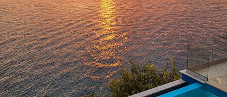 A poolside view overlooking a body of water with a sunset in the background.