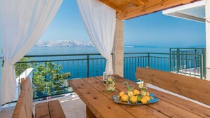 Eine Holzterrasse mit gedecktem Tisch, mit Blick auf ein Gewässer und eine entfernte Küstenlinie.