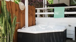Un jacuzzi en un patio trasero con valla de madera, barandal blanco y una toalla verde colgada.