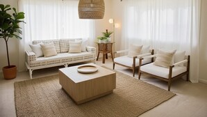 Una sala de estar con un sofá, dos sillones, una mesita de centro, una lámpara colgante y una planta en maceta.