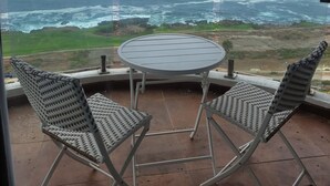 Un balcón con una mesa y dos sillas, con vista al litoral, el océano y terreno rocoso.