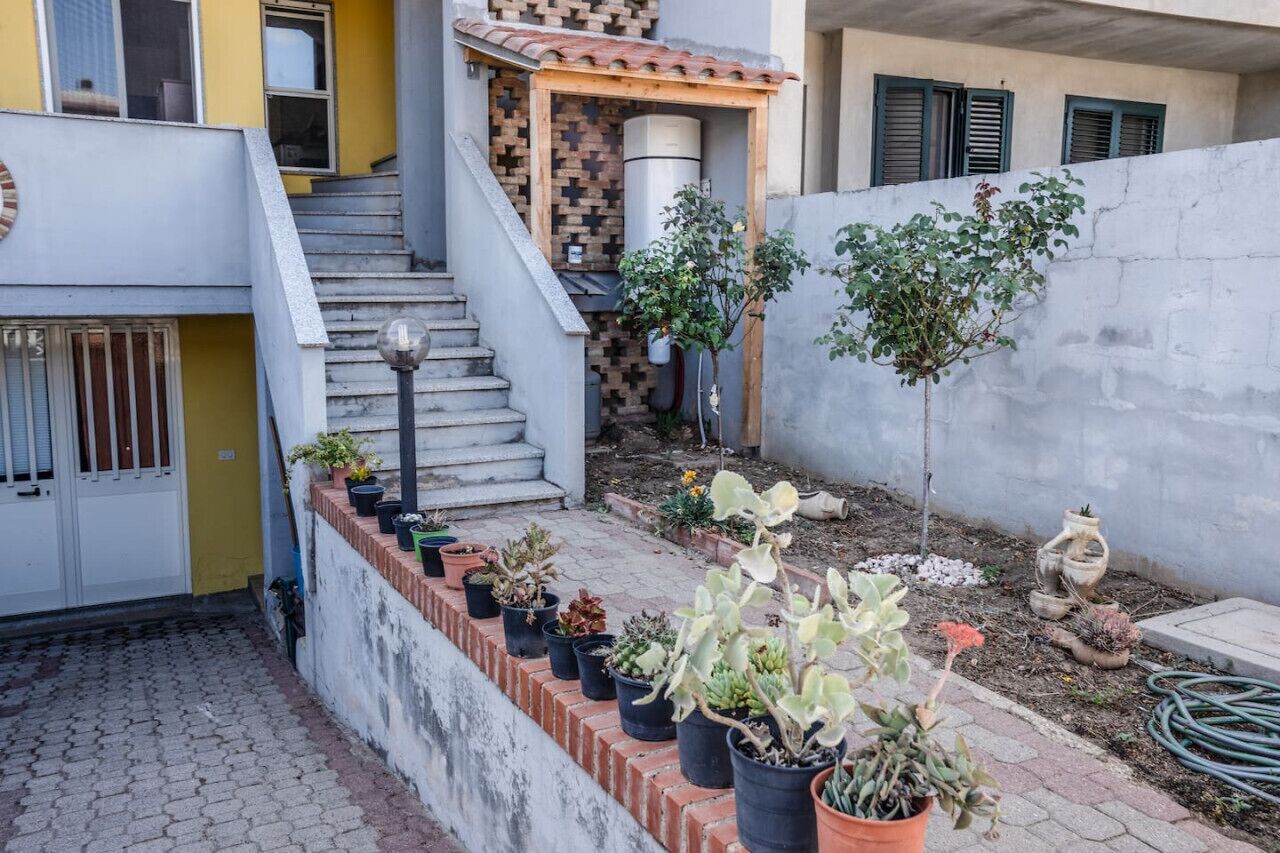 Ein Wohnhof mit einer Ziegelstiege, die zu einer Tür führt, mit Kübelpflanzen und einer kleinen Gartenanlage.