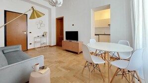 Ein modernes Wohnzimmer mit Sofa, Couchtisch, Fernseher und einem Essbereich mit Stühlen und Tisch.