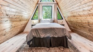 Kolmionmuotoinen huone, jossa on puulattia, sänky, kaksi yöpöytää ja ikkuna.