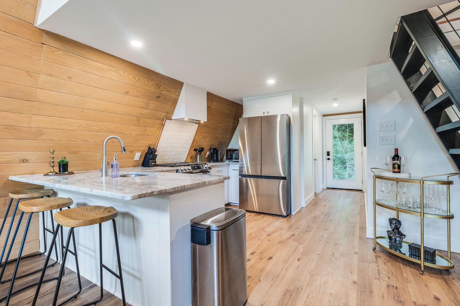 Una cocina moderna con una isla central, electrodomésticos de acero inoxidable y una pared de acento de madera.