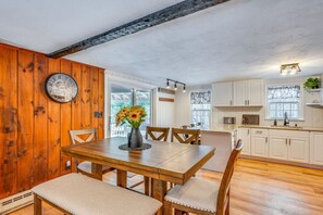 Ein Essbereich mit Holztisch und Stühlen, einer Vase mit Blumen und einer Uhr an der Wand.