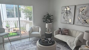 A modern living room with a large window, a round coffee table, two white sofas, and abstract wall art. - Spacious Apartment in Prime West Hollywood - Steps from Restaurants & Night life (Los Angeles)
