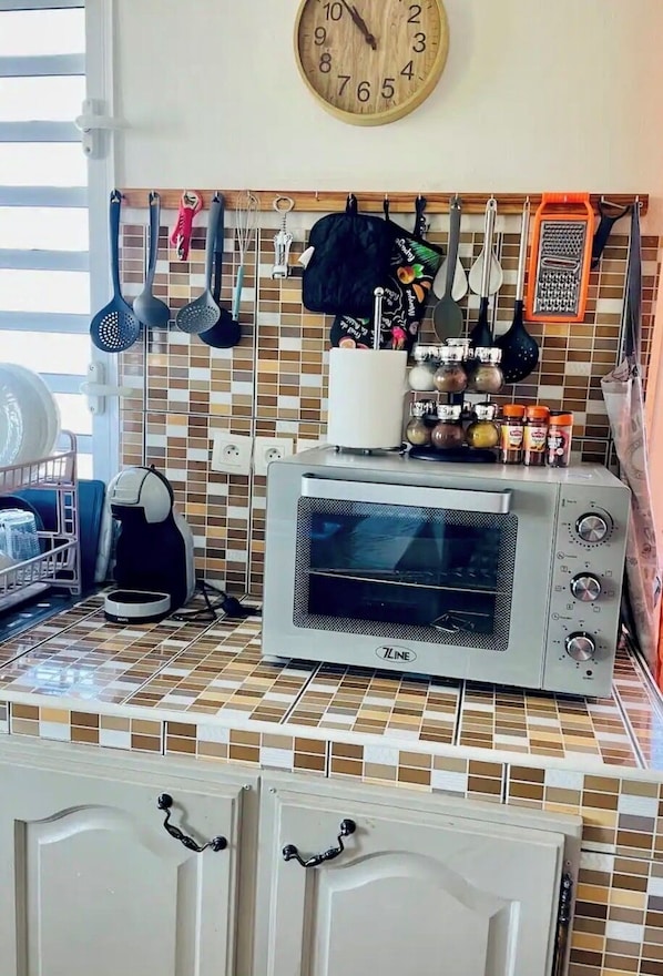 A kitchen with a microwave, a toaster oven, and a clock on the wall. - Gîte Délia (Saint-Louis)