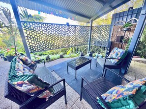 Un patio al aire libre con mobiliario de mimbre, cerca decorativa y plantas en macetas.