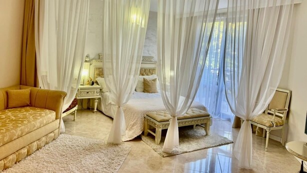 A bedroom with a bed, a nightstand, a lamp, a sofa, and sheer curtains. - Luxury Coastal Dreams Apartment (Свети Влас)