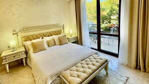 A spacious bedroom with a large bed, a bench, a nightstand, and a view of the outdoors through a sliding glass door. - Luxury Coastal Dreams Apartment (Свети Влас)