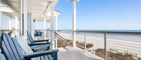 A covered deck with blue Adirondack chairs overlooking a beach.