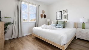 A bedroom with a wooden bed, white bedding, a nightstand with a lamp, a window with curtains, and a ceiling fan. - Front Beach Condo! 1 Block to Center Street-3C (Folly Beach)