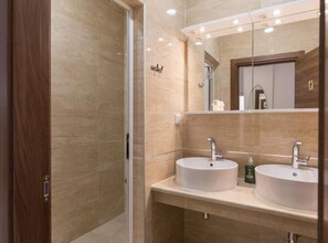 Un baño moderno con dos lavamanos, cabina de ducha de vidrio y un espejo grande.