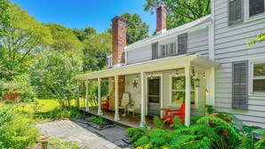 A covered porch with outdoor seating, a brick chimney, and lush greenery. - Historic Catskills Farmhouse: Ski, Hike & Relax! (Catskill)