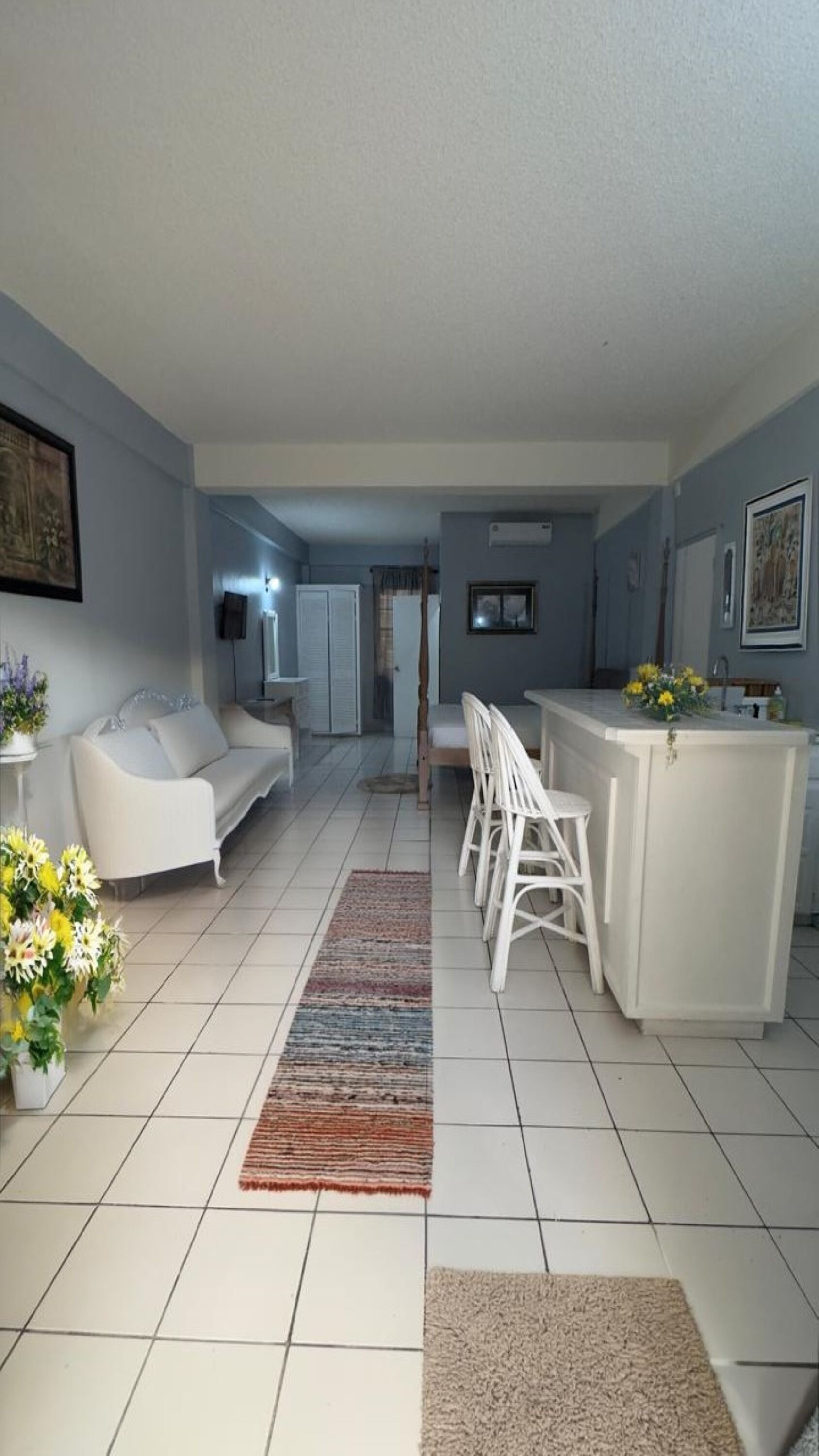 Un salon moderne avec un canapé blanc, un coin repas avec des chaises blanches, un îlot de cuisine et un sol carrelé.