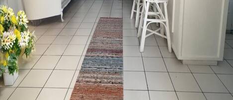 Un salon moderne avec un canapé blanc, un coin repas avec des chaises blanches, un îlot de cuisine et un sol carrelé.